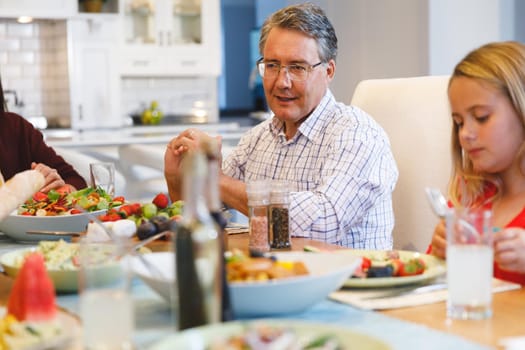 Caucasian grandfather and granddaughter sitting at table and having family dinner. family spending time together at home.