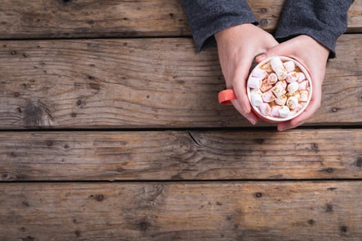 Overhead view of female hands holding mug of hot chocolate drink with copy space at table in cafe. lifestyle and cafe culture.