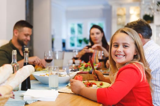 Portrait of caucasian grandfather and parents with daughter sitting at table having dinner. family spending time together at home.