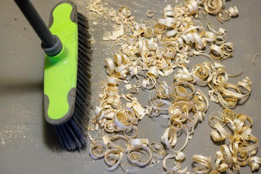 a small pile of wood shavings on a gray linoleum floor with plastic broom brush