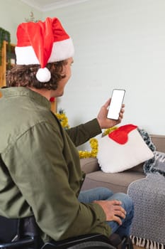 Caucasian disabled man in santa hat using smartphone with copy space at home during christmas. christmas festivity and celebration concept