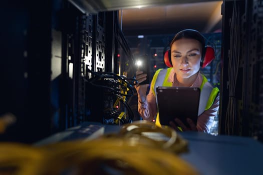 Caucasian female engineer using smartphone flash while inspecting the server in computer server room. database server management and maintenance concept