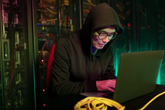 Asian male hacker using a laptop in computer server room. cyber crime and hacking concept