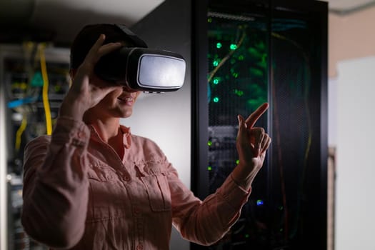 Caucasian woman wearing vr headset touching an invisible screen in computer server room. database server and futuristic technology concept