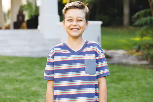 Portrait of smiling caucasian boy outside house looking at camera in garden. spending time at home.