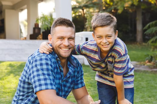 Portrait of smiling caucasian father and son embracing outside house in garden. family spending time at home.