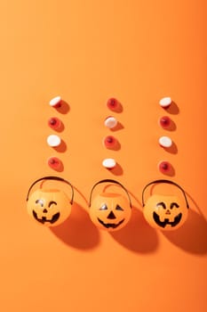 Halloween candies and three pumpkin shaped buckets against orange background. halloween festivity and celebration concept