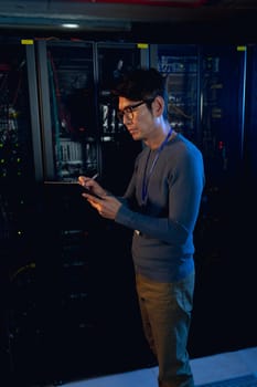 Asian male engineer writing on clipboard in computer server room. database server management and maintenance concept