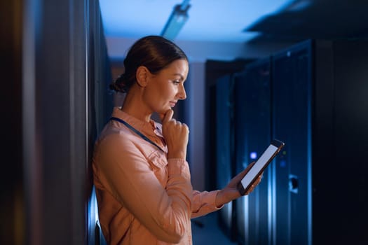 Thoughtful caucasian female engineer using digital tablet in computer server room. database server management and maintenance concept