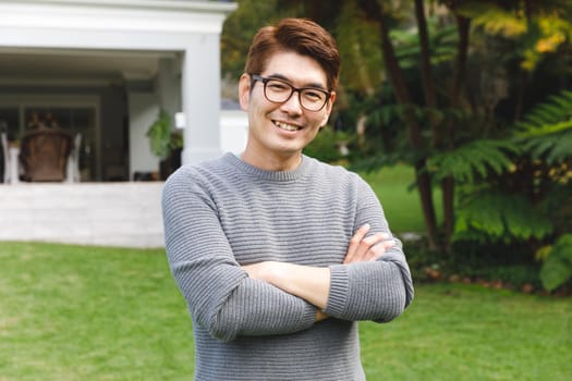 Portrait of happy asian man wearing glasses smiling in garden outside family home. enjoying leisure time alone at home.