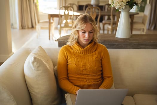 Caucasian woman sitting on couch in luxury living room using laptop, concentrating. spending free time at home with technology.