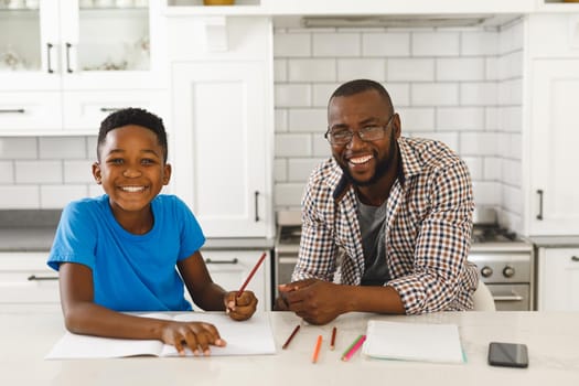 Portrait of smiling african american father and his son in kitchen, doing homework together. family spending time at home.