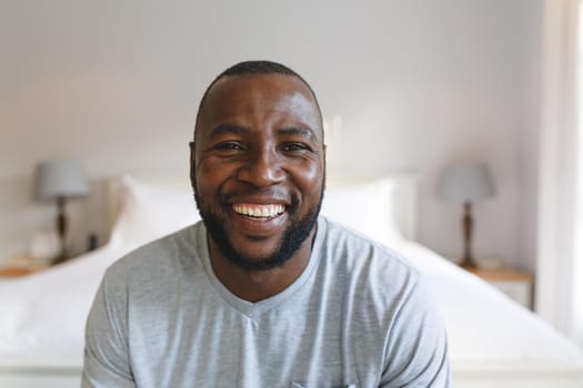 Portrait of happy african american man looking at camera and smiling in bedroom. spending time alone at home.