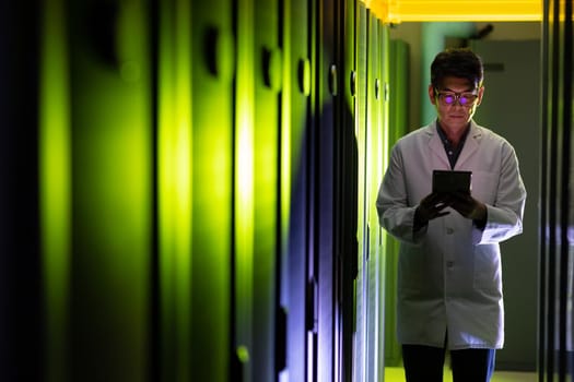 Asian male engineer wearing an apron using digital tablet while inspecting in computer server room. database server management and maintenance concept