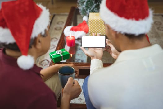Biracial adult son and senior father in santa hats making smartphone christmas video call. christmas, festivity and communication technology.