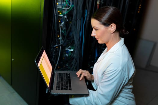 Caucasian female engineer wearing an apron using laptop while inspecting in computer server room. database server management and maintenance concept