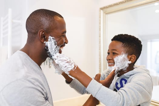 African american father with son having fun with shaving foam in bathroom. family spending time at home.