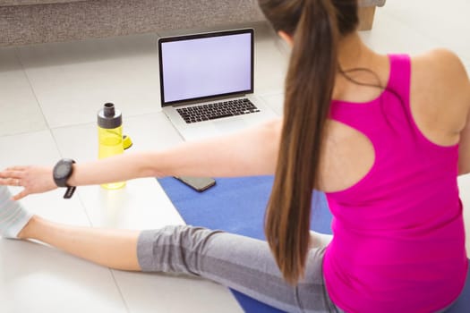 Back view of woman exercising at home with laptop with copy space on screen. healthy active lifestyle and fitness at home.