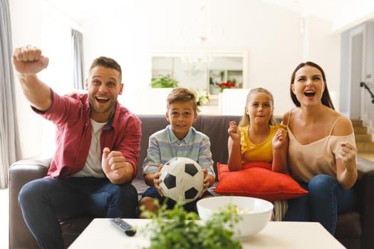 Excited caucasian parents on couch with daughter and son watching football match on tv and cheering. family entertainment and leisure time together at home.