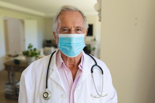 Portrait of senior caucasian male doctor wearing face mask looking at camera. medicine and healthcare services during covid 19 pandemic concept.