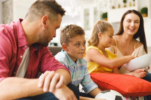 Happy caucasian parents, daughter and son sitting on couch talking and watching football match in tv. family entertainment and leisure time together at home.