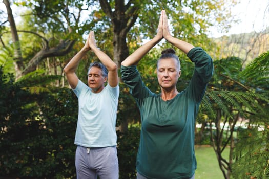 Happy senior caucasian couple practicing yoga, meditating in sunny garden. healthy retirement lifestyle, spending time at home.