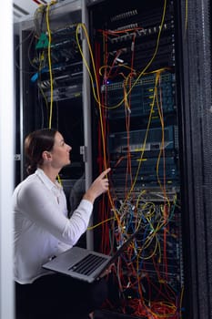Caucasian female engineer with laptop inspecting computer server in computer server room. database server management and maintenance concept