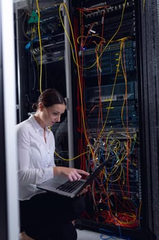 Caucasian female engineer with laptop inspecting computer server in computer server room. database server management and maintenance concept