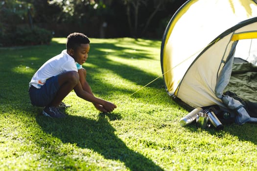 African american boy having fun pitching tent with ropes in sunny garden. spending time at home.