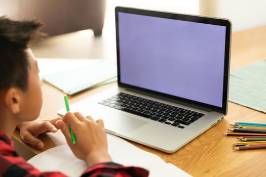 Asian boy using laptop with blank screen at home. domestic lifestyle and online education during covid 19 pandemic concept.