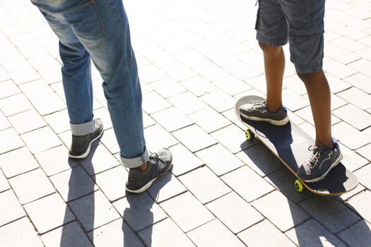 Low section of african american father with son skateboarding on sunny day in garden. family spending time at home.