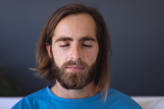 Caucasian man sitting on sofa meditating with eyes closed. staying at home in isolation during quarantine lockdown.