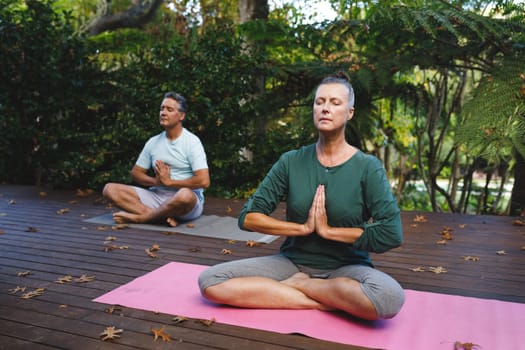 Happy senior caucasian couple practicing yoga, meditating in sunny garden. healthy retirement lifestyle, spending time at home.