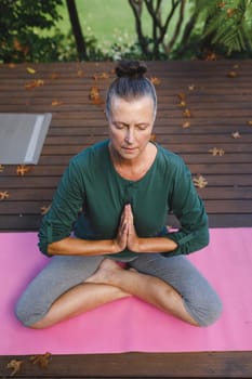 Happy senior caucasian woman practicing yoga, meditating in sunny garden. healthy retirement lifestyle, spending time at home.