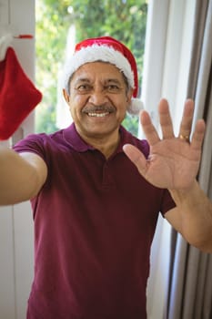 Portrait of happy biracial senior man in santa hat making christmas video call. christmas, festivity and communication technology.