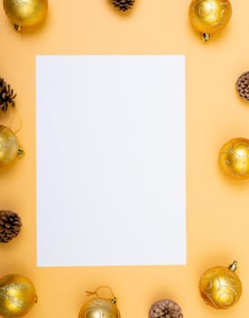 Composition of white card with copy space framed with baubles and pine cones on yellow background. christmas, tradition and celebration concept.