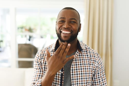 Portrait of african american man smiling and looking at camera in living room talking sign language. communication without words.