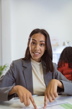 Smiling biracial businesswoman sitting at desk making video call in modern office. business and office workplace.