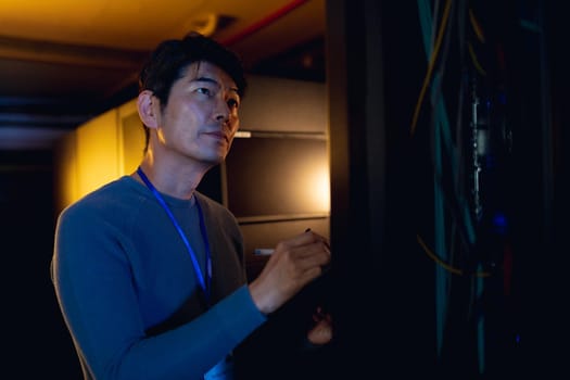 Asian male engineer writing on clipboard while inspecting in computer server room. database server management and maintenance concept