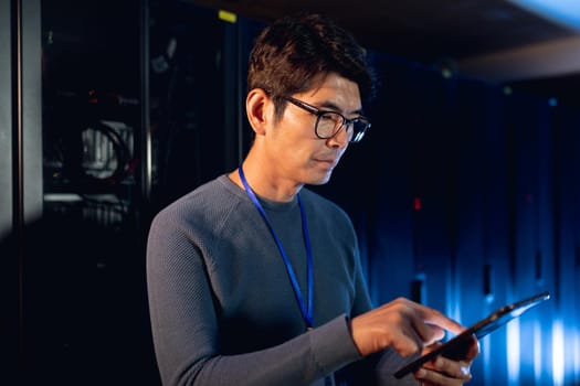 Asian male engineer using digital tablet in computer server room. database server management and maintenance concept
