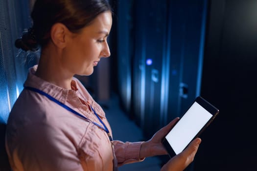 Caucasian female engineer using digital tablet with copy space in computer server room. database server management and maintenance concept