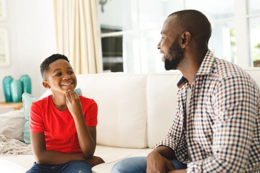 Happy african american father with son sitting on couch in living room talking sign language. father and son communicating without words.