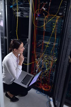 Thoughtful caucasian female engineer with laptop inspecting computer server in computer server room. database server management and maintenance concept