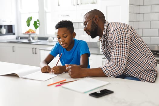 African american father and son in kitchen, doing homework together. family spending time at home, father son relationship.