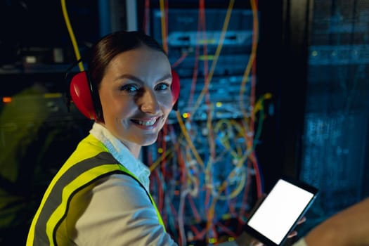 Portrait of caucasian female engineer smiling while using digital tablet in computer server room. database server management and maintenance concept