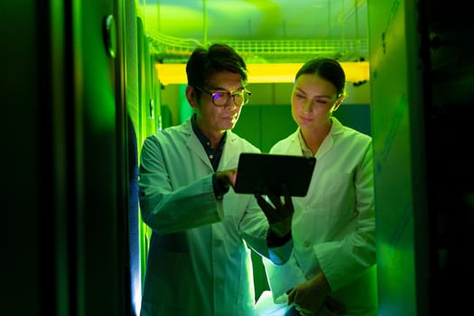 Diverse male and female engineers wearing aprons using digital tablet in computer server room. database server management and maintenance concept
