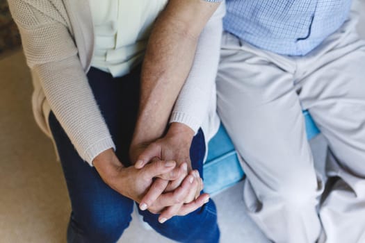 Senior caucasian couple sitting on sofa and holding hands. retirement lifestyle, spending time at home.