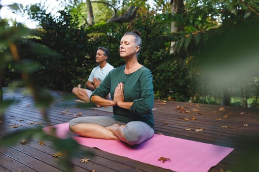 Happy senior caucasian couple practicing yoga, meditating in sunny garden. healthy retirement lifestyle, spending time at home.