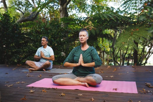 Happy senior caucasian couple practicing yoga, meditating in sunny garden. healthy retirement lifestyle, spending time at home.