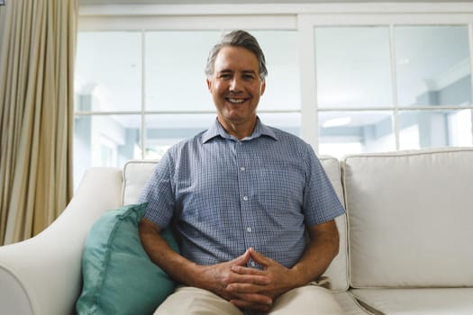 Happy senior caucasian man in living room, sitting on sofa smiling during video call. retirement lifestyle, spending time at home with technology.